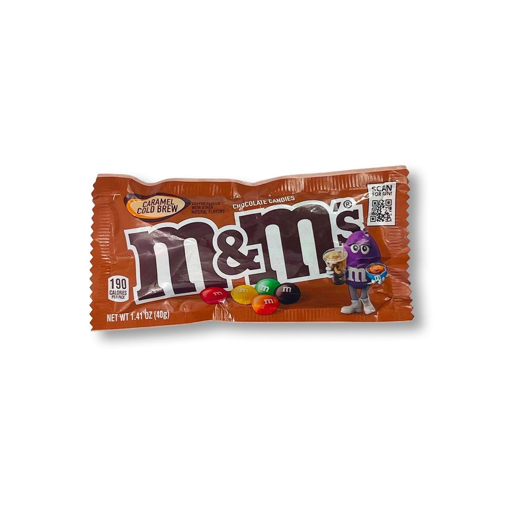 Un paquet brun sur fond blanc avec sur le devant 5 M&M’s de rouge, jaune, vert, marron et orange et à droite un bonhomme en M&M’s mauve qui tient une boisson froide 