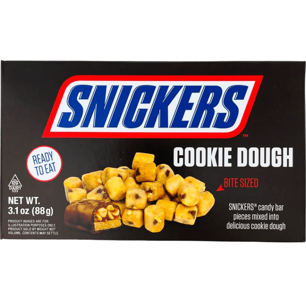 Un carton noir sur fond blanc avec écrit en grand au-dessus « Snickers » en bleu et en bas la moitié d’un Snickers et à l’arrière des carrés de cookie dough avec des pépites de chocolat et des morceaux de cacahuètes