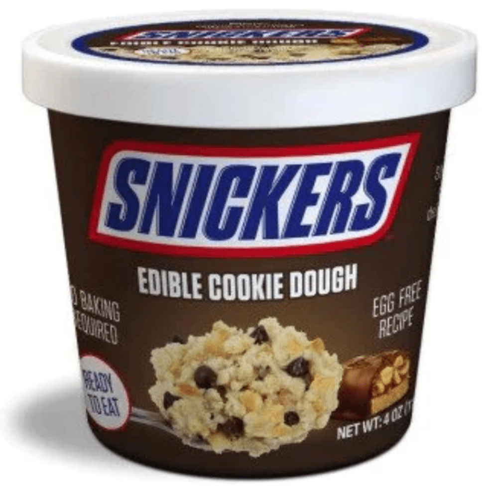 Un emballage en bol marron sur fond blanc avec écrit en grand au-dessus « Snickers » en bleu et en bas il y a du cookie dough avec des pépites de chocolat et des morceaux de cacahuètes