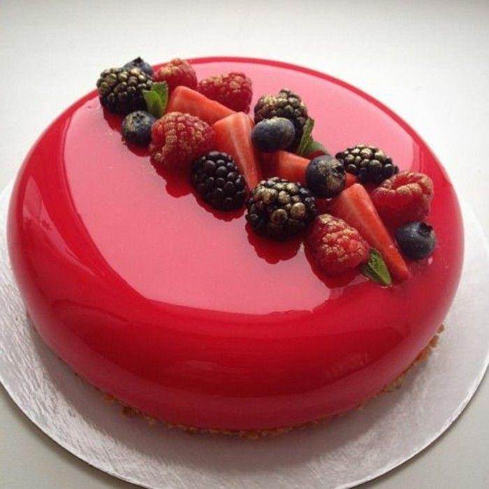 Un gâteau rouge sur une planche grise avec sur le dessus des framboise, fraise et mure