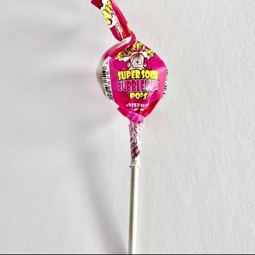 Une sucette sur fond blanc avec un bâtonnet blanc et un emballage rose avec un visage qui a la tête qui explose