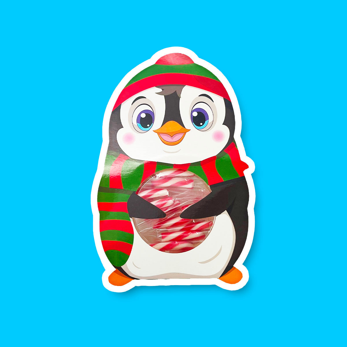 Un pingouin sur fond bleu en bonnet et écharpe à stries rouges et vertes, avec un ventre transparent qui dévoile les cannes à sucre rouges et blanches