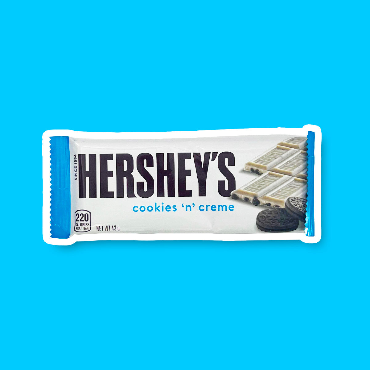 Un paquet blanc avec à droite une barre chocolatée Hershey’s Cookies & Cream et sur le devant 2 cookies noirs, le tout sur un fond bleu