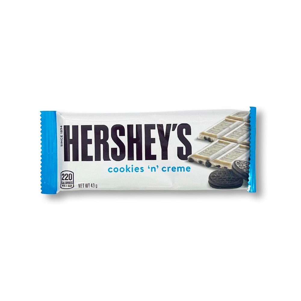 Un paquet blanc avec à droite une barre chocolatée Hershey’s Cookies & Cream et sur le devant 2 cookies noirs, le tout sur un fond blanc