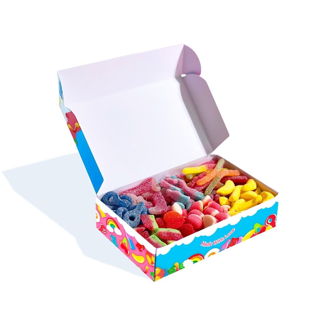 Un carton bleu et rose ouvert contenant des bonbons en forme de sucettes, dents de vampire, bananes, bout de pastèque, le tout sur fond blanc