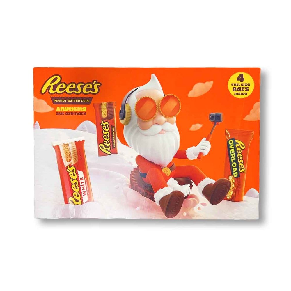 Un emballage orange sur fond blanc avec un père Noël stylé qui se filme entrain de descendre une montage enneigée assis sur un chocolat Reese’s géant et il y a 3 paquet de chocolat dans la neige