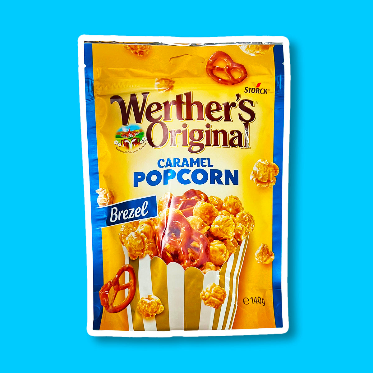 Un emballage de couleur orange et aux extrémités bleues, avec un paquet de popcorn au caramel et bretzel. Sur le côté gauche, il y une étiquette bleu « Brezel » le tout sur fond bleu