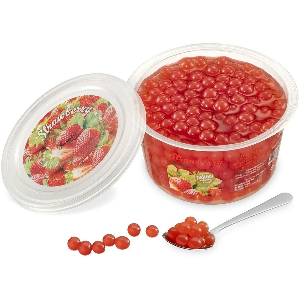 Une boite sur fond blanc remplie de perles rouges et à gauche le couvercle avec plusieurs fraises. Devant des perles rouges dans une cuillère