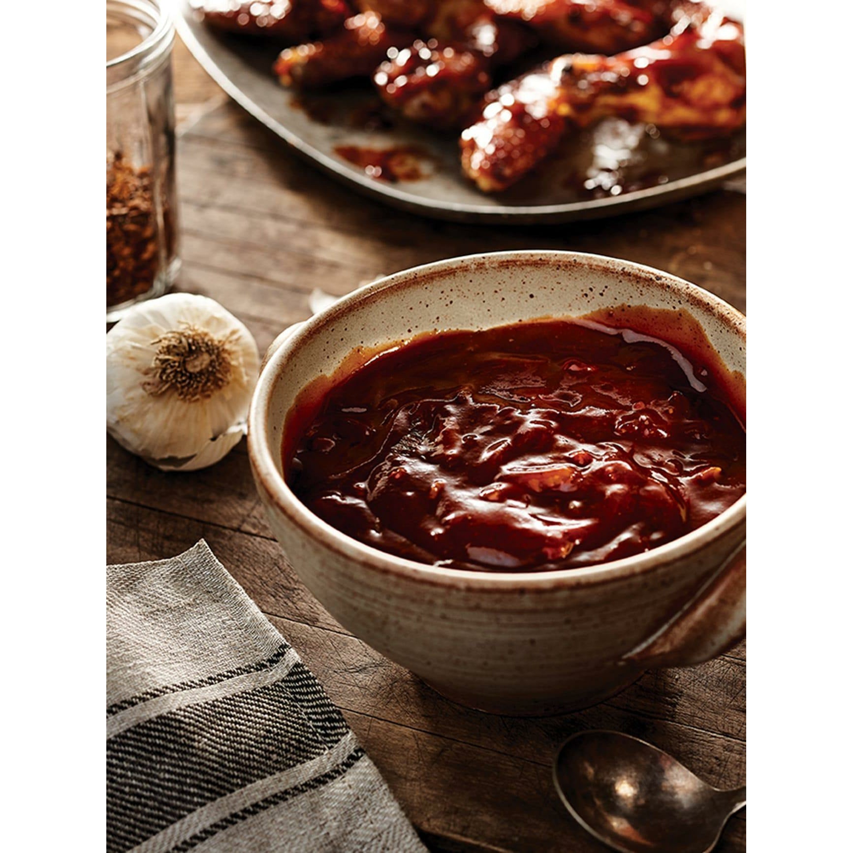 Un bol avec une sauce rouge, à coté une gousse d’ail et à l’arrière du poulet avec une sauce rouge. Le tout sur une table en bois 