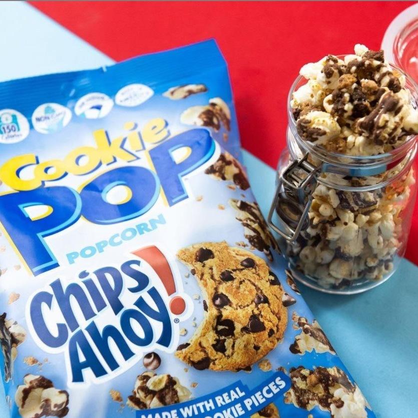 Un paquet bleu avec plein de popcorn au chocolat et à droite un bocal transparent rempli de popcorns, sur un table bleu et rouge