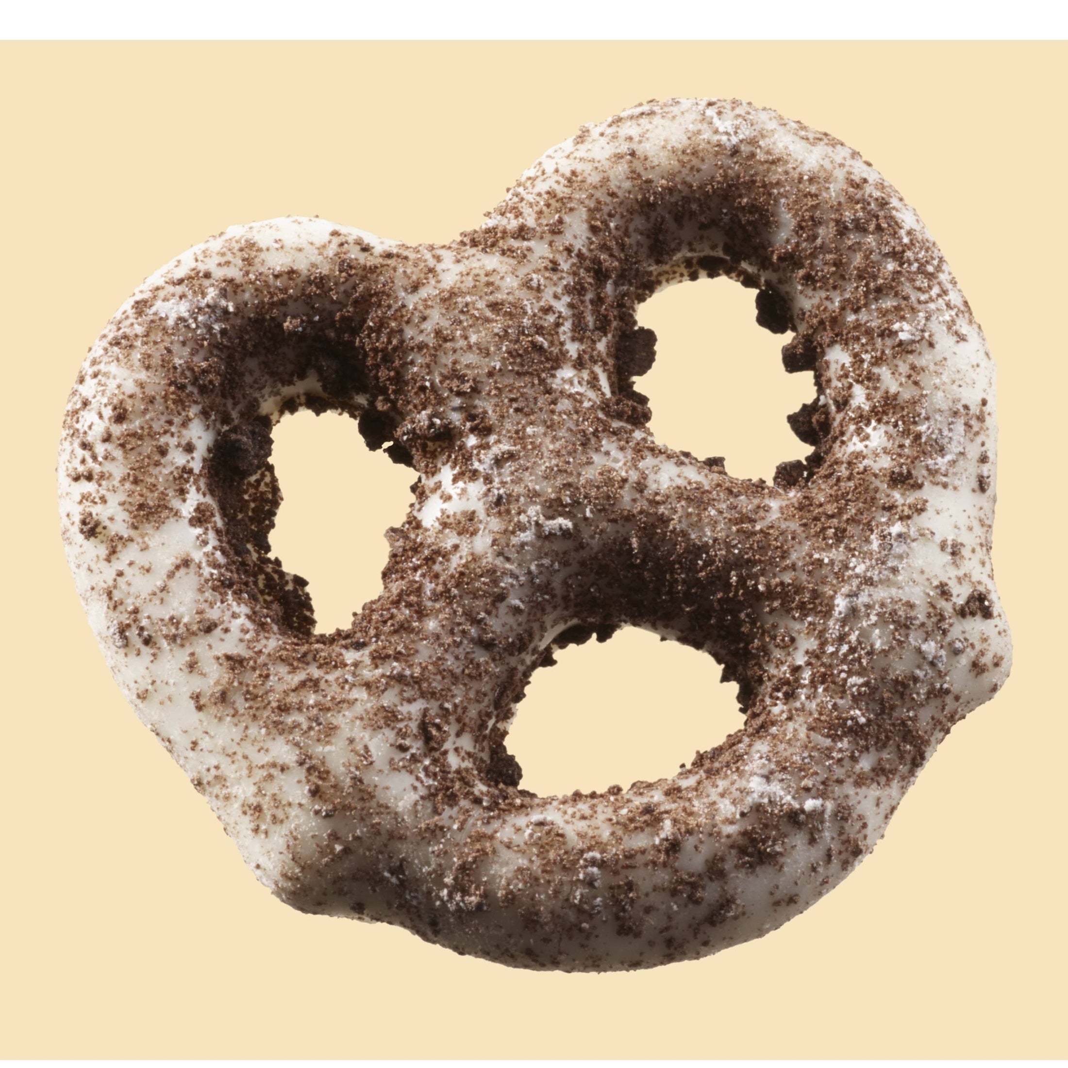 Un bretzel enrobé de chocolat blanc et saupoudrés poudre de cookies au chocolat sur un fond beige