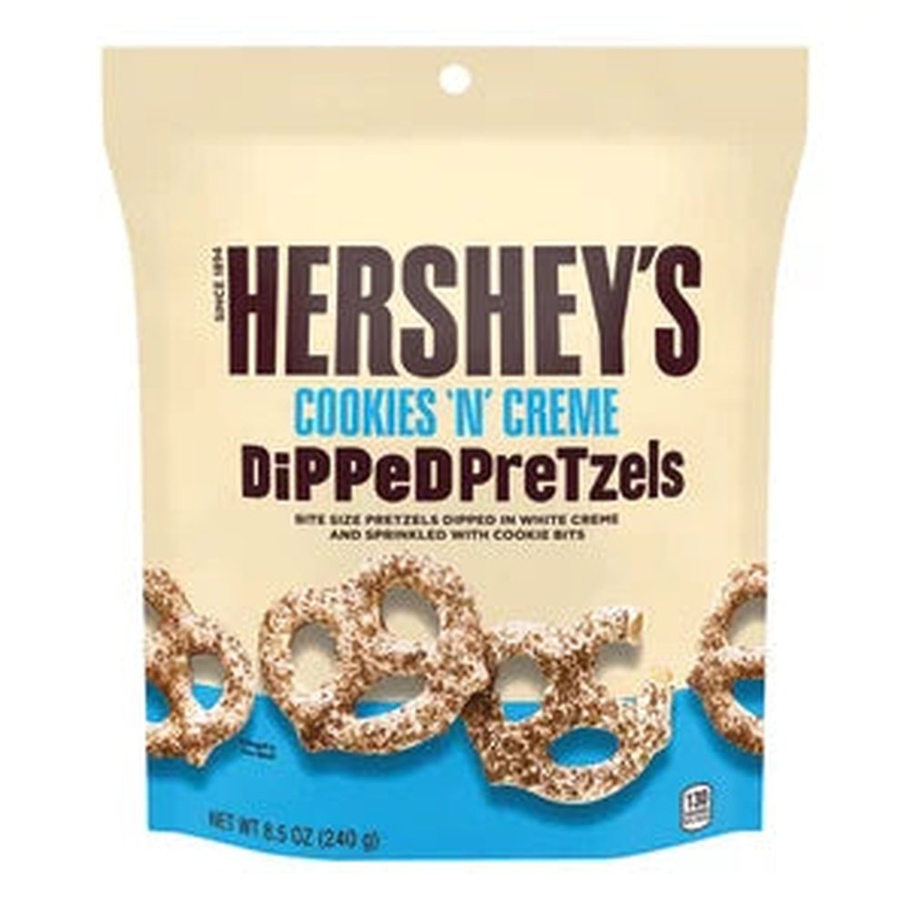 Un emballage beige avec une bande bleu en bas, et des bretzels enrobés de chocolat blanc et saupoudrés poudre de cookies au chocolat, le tout sur fond blanc 