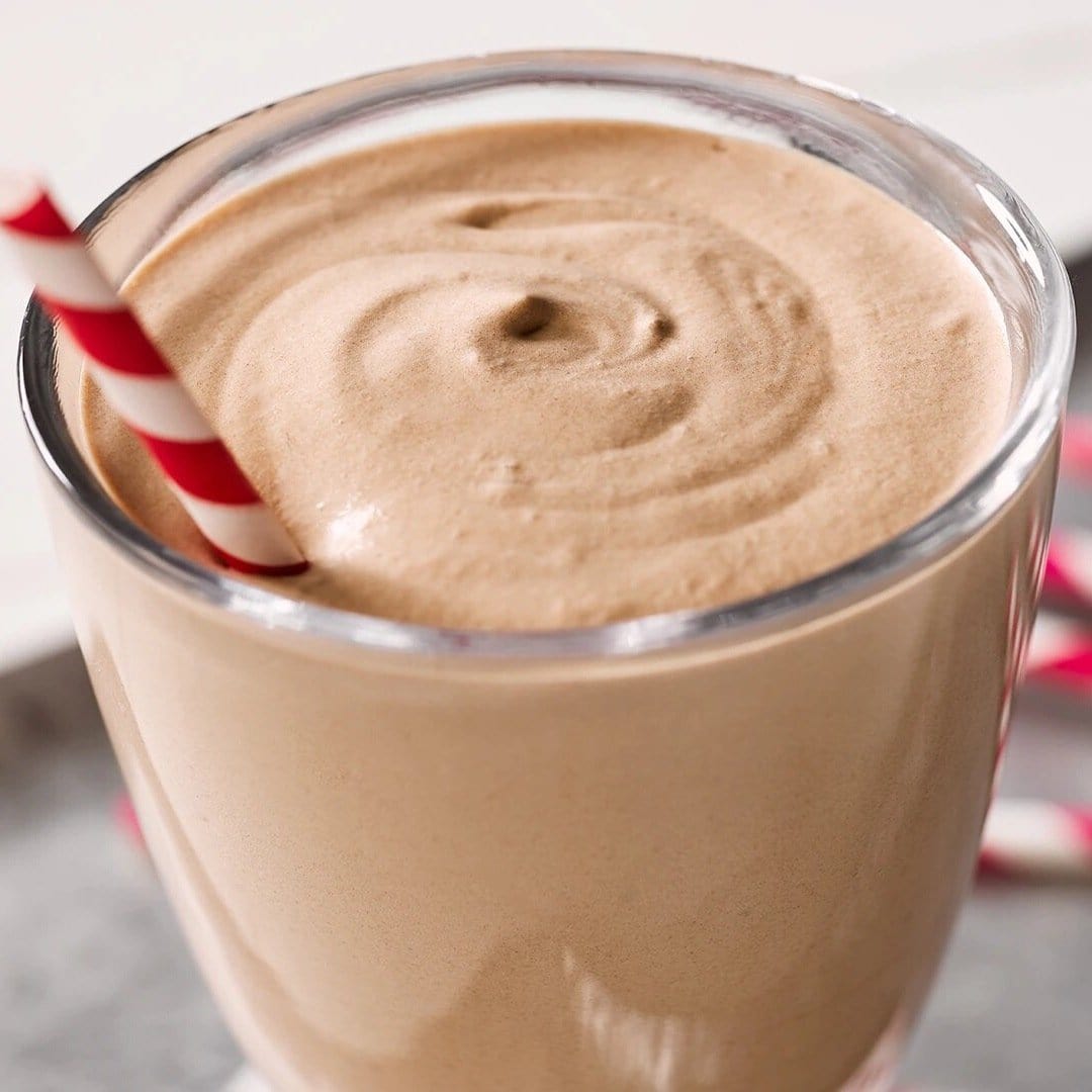 Une tasse en verre transparent avec une chocolat glacé et une paille rayé rouge-blanc