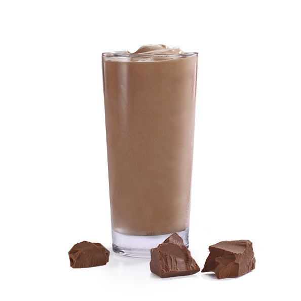 Un verre transparent rempli d’une mousse brune sur fond blanc et devant 3 grandes pépites de chocolat