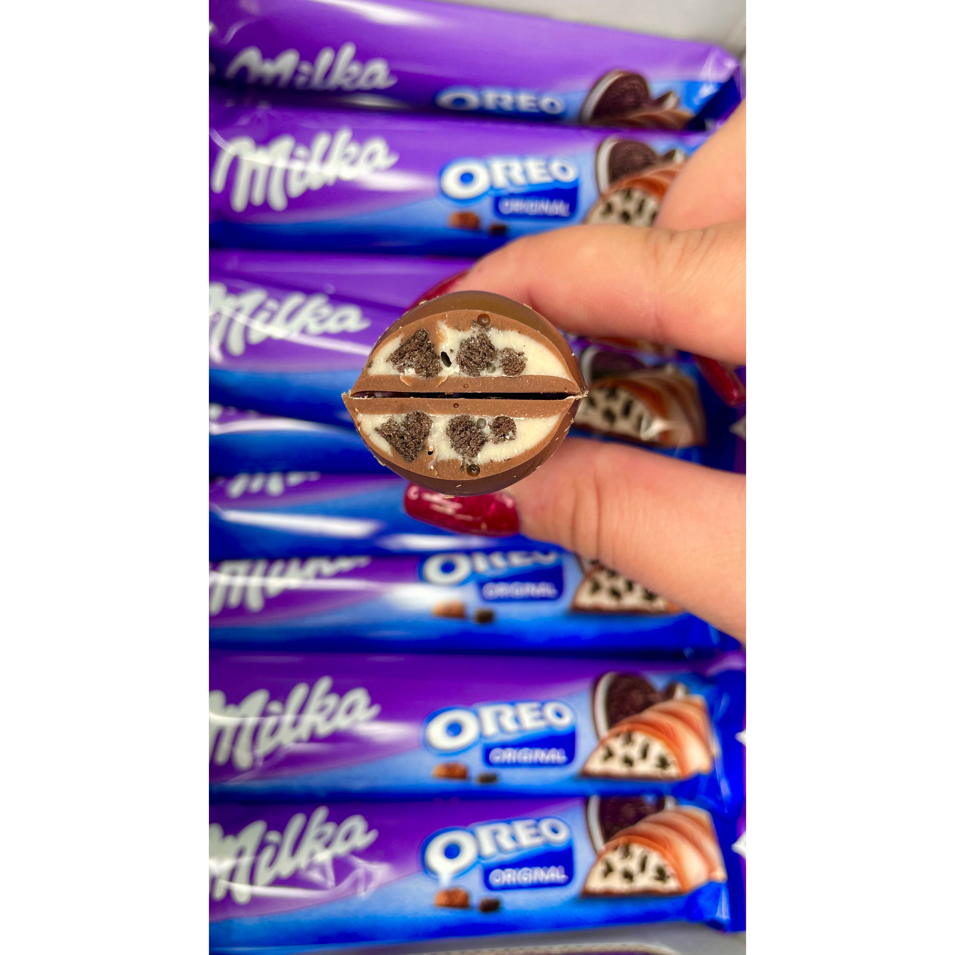 Plusieurs emballages du Milka Oreo Bar avec en premier plan une main qui tient une barre chocolatée coupée en 2 et dévoile son intérieur 