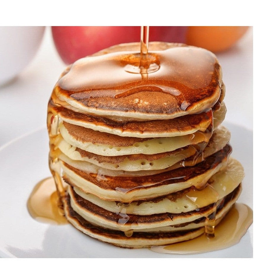 Une assiette blanche avec des pancakes, du sirop brun et un petit bol blanc avec une confiture rouge. Le tout sur une table blanche