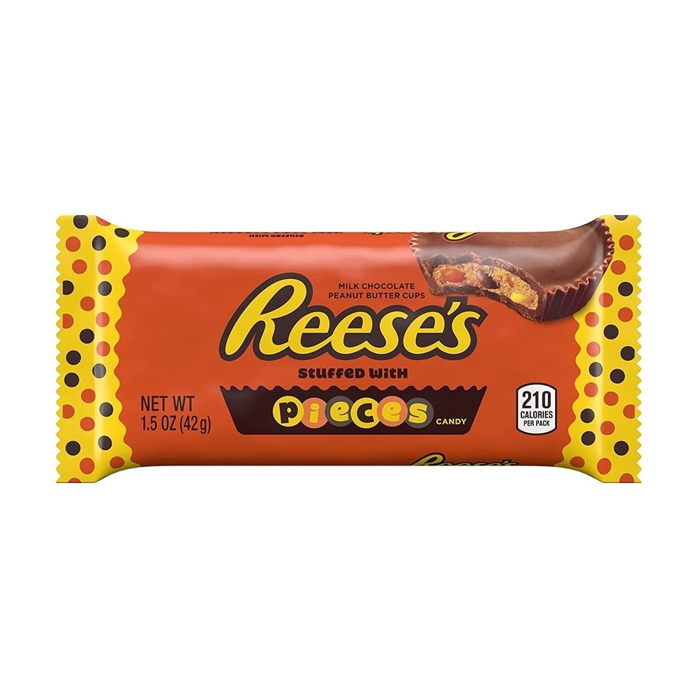 Un emballage orange avec des extrémités jaunes sur fond blanc avec écrit « Reese’s » à gauche et à droite il y a un chocolat en cup qui est croqué et on y voit une pâte brune claire avec des morceaux colorés 