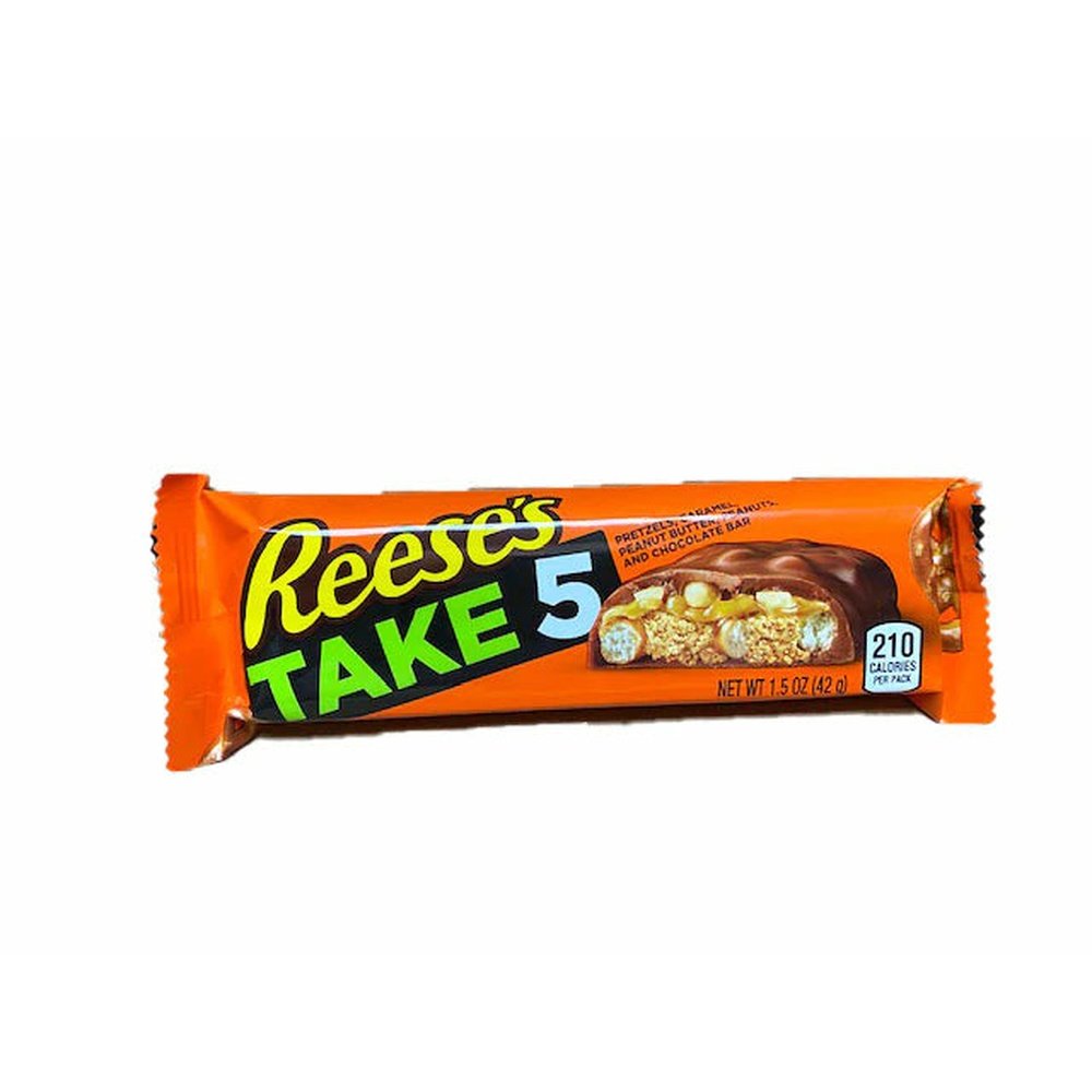 Un emballage orange sur fond blanc avec une barre de chocolat coupé, à l’intérieur on y voit des bretzels, des cacahuètes et du caramel