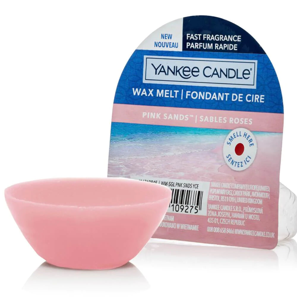 Un emballage sur fond blanc avec une plage avec du sable rose et devant il y a un petit bol de cire rose